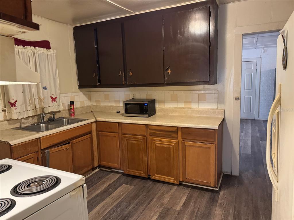 A kitchen features dark upper cabinets, wood lower cabinets, a microwave, and a double sink — 1049 PLATEAU AVENUE, LAKELAND, FL
