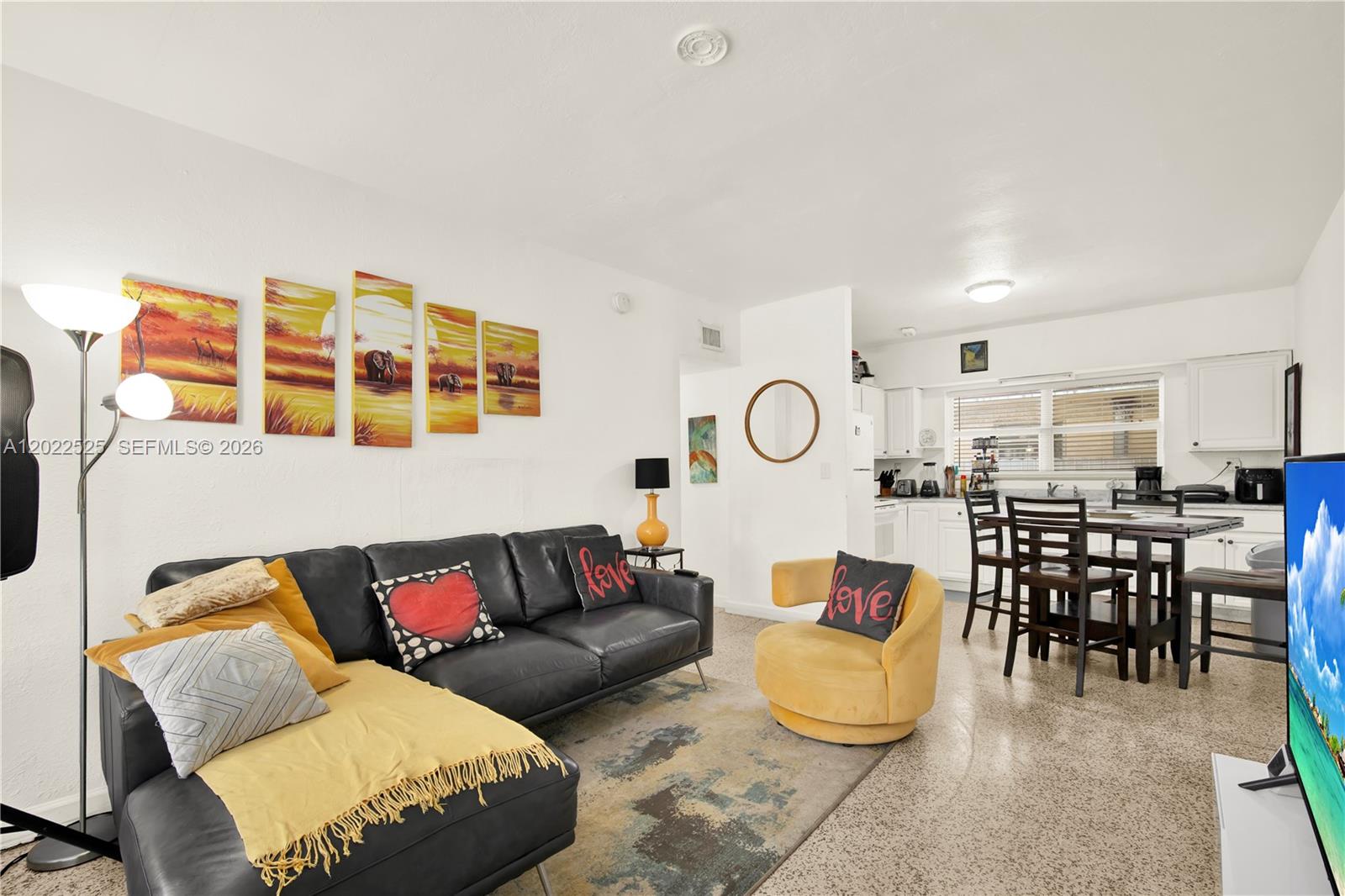 A living room with a black sectional sofa, yellow chair, and an open kitchen area — 1236 NE 109th St # 2, Miami FL 33161, MIAMI, FL