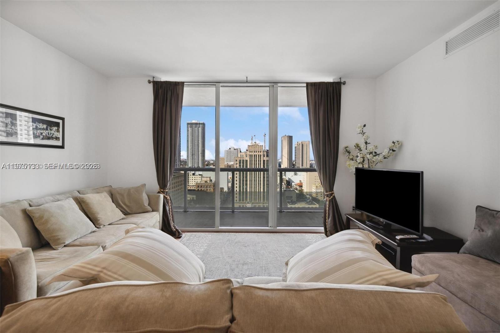 A living room features a beige sectional sofa, a television, and a balcony with city views — 50 Biscayne Blvd # 2111, Miami FL 33132, MIAMI, FL