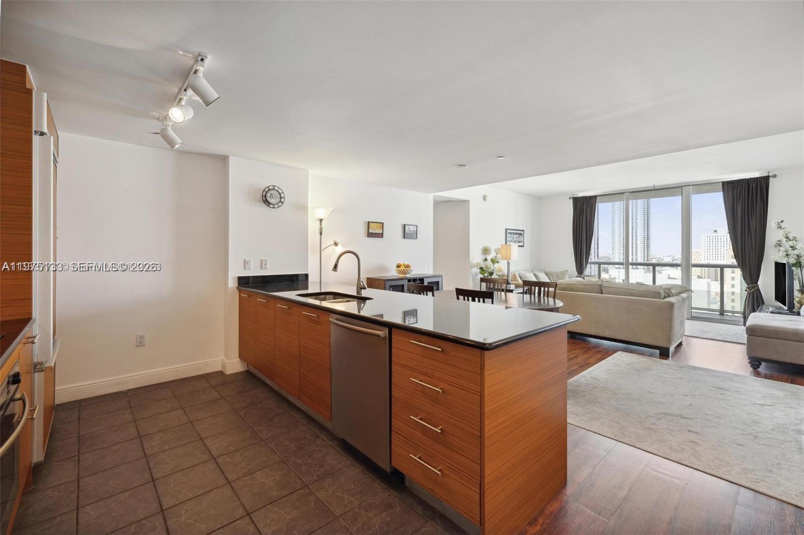 A modern kitchen with wood cabinets and a black countertop opens into a living area — 50 Biscayne Blvd # 2111, Miami FL 33132, MIAMI, FL