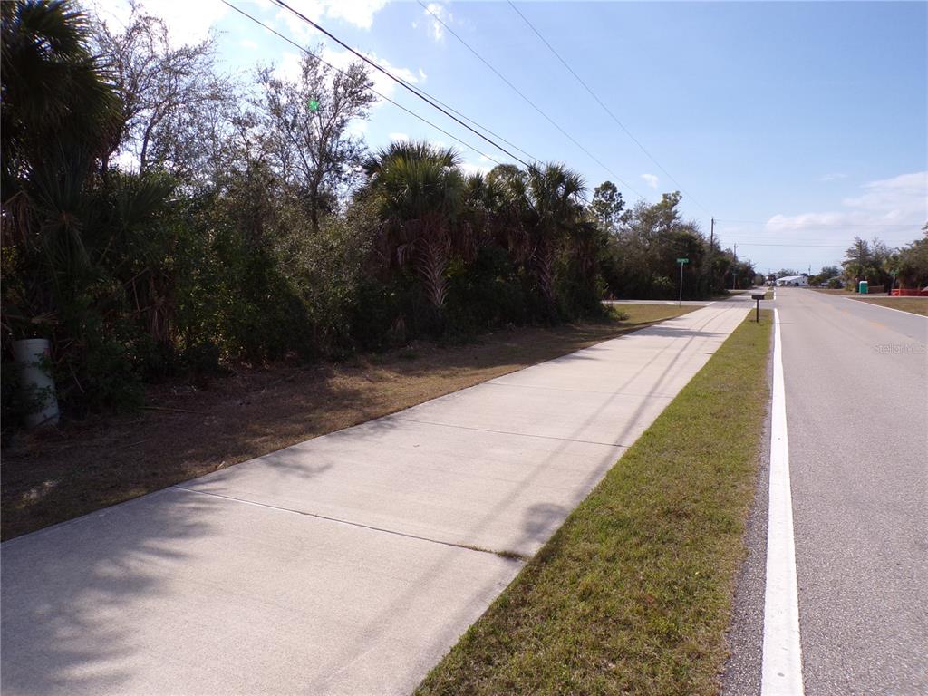 A paved sidewalk runs alongside a road next to a wooded lot with palm trees — 14589 KEYSTONE BOULEVARD, PORT CHARLOTTE, FL