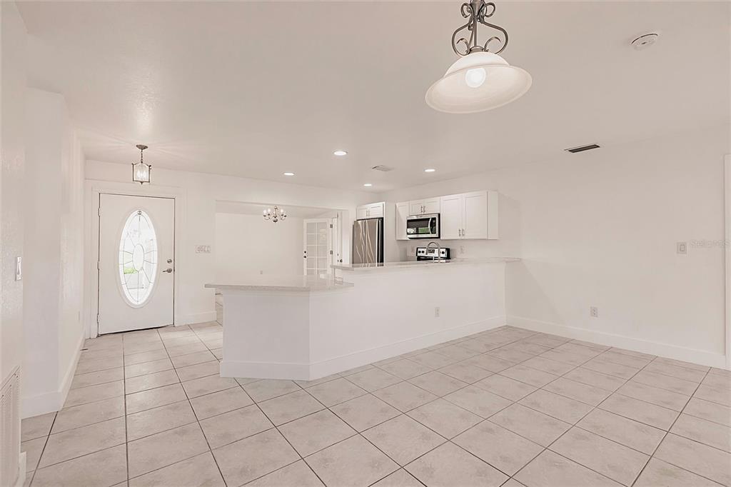 A bright, open-concept kitchen and entryway featuring white cabinetry, a breakfast bar, and tiled flooring — 3129 BUTTONWOOD PLACE, PUNTA GORDA, FL