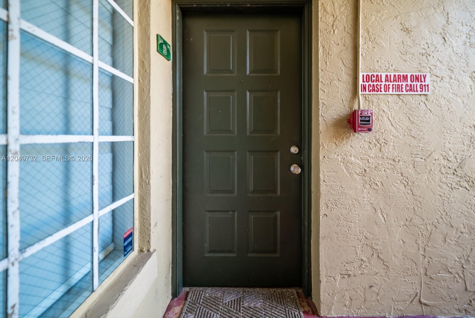 A dark green door with a fire alarm and sign on the adjacent textured wall — 18308 NW 68th Ave # B, Hialeah FL 33015, HIALEAH, FL