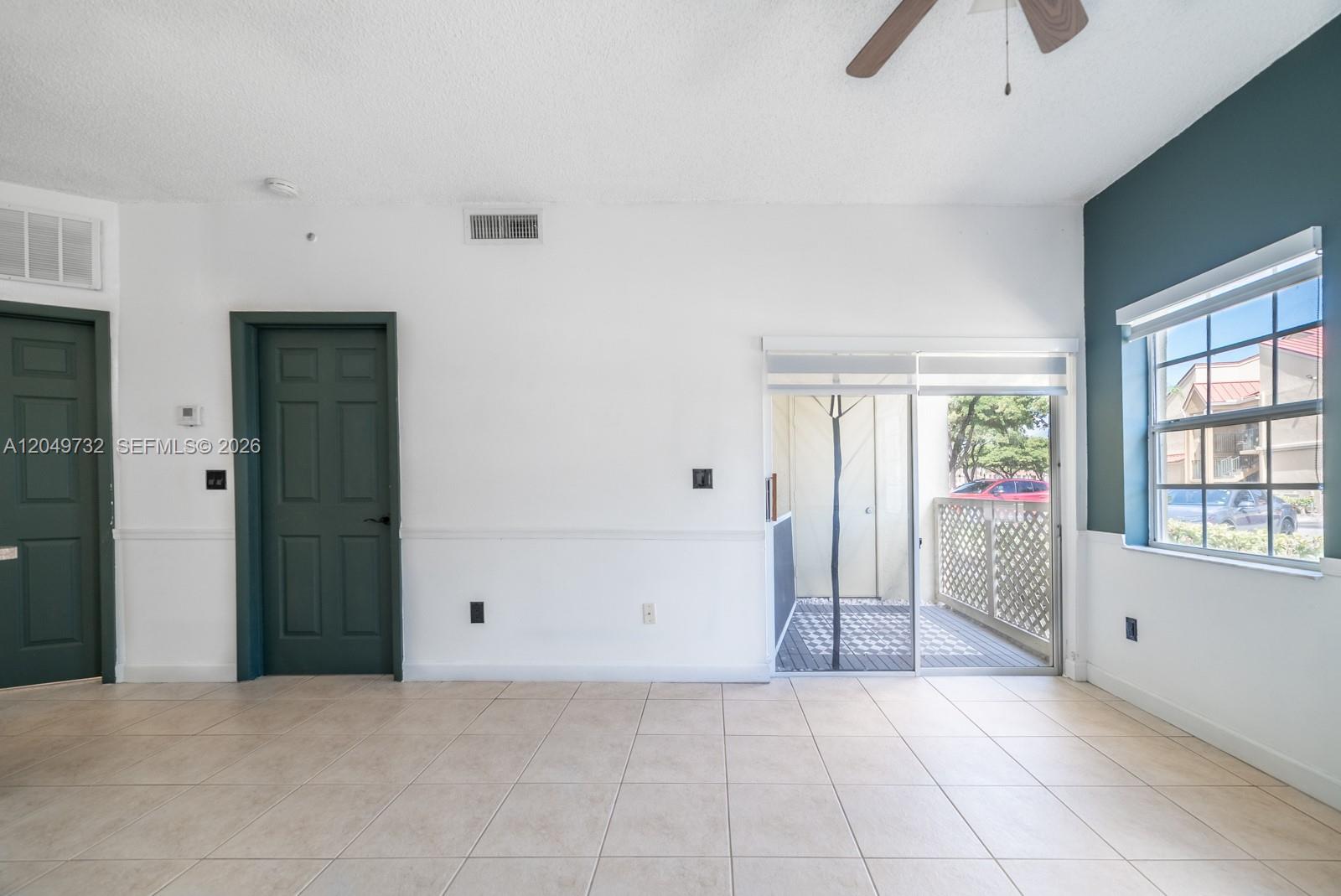 A room with tiled floors, two dark green doors, and a sliding glass door to a patio — 18308 NW 68th Ave # B, Hialeah FL 33015, HIALEAH, FL