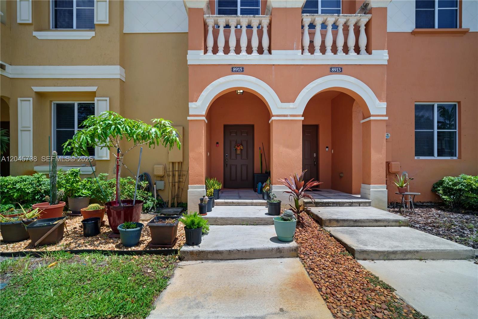 The exterior of a two-story townhouse features arched entryways, a stone balcony, and potted plants — 8915 SW 19th St, Miramar FL 33025, MIRAMAR, FL