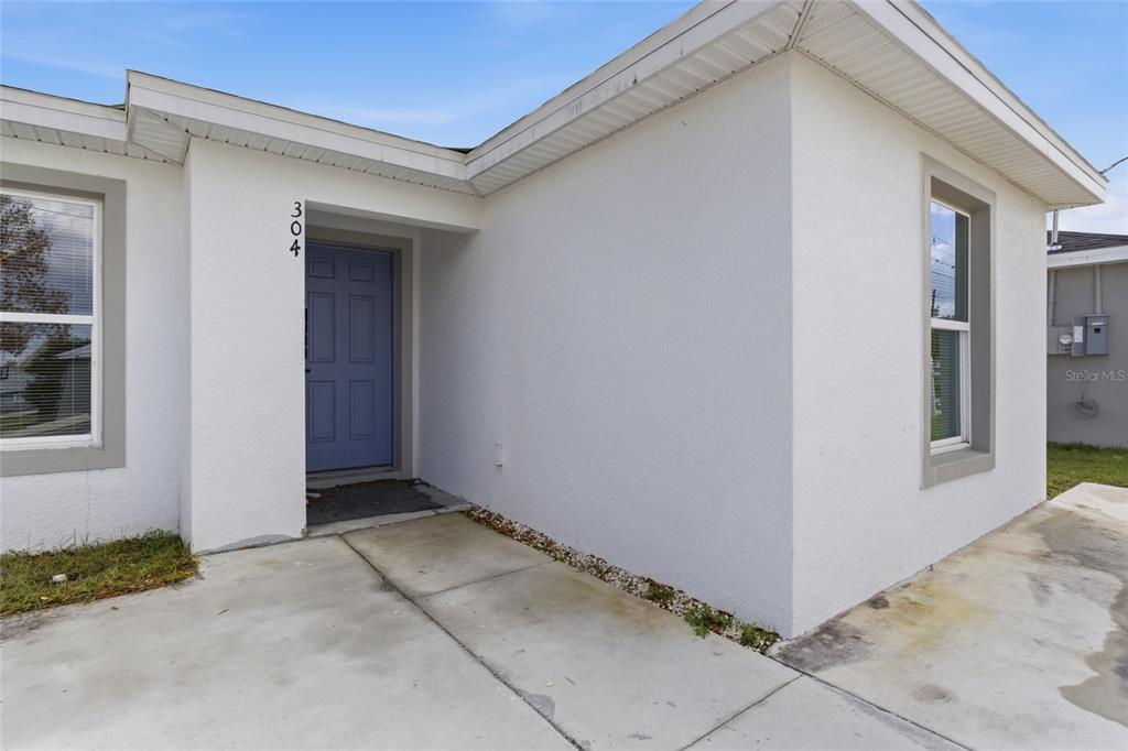 The exterior of a white house features a blue front door and a concrete walkway — 302 AVENUE P NW, WINTER HAVEN, FL