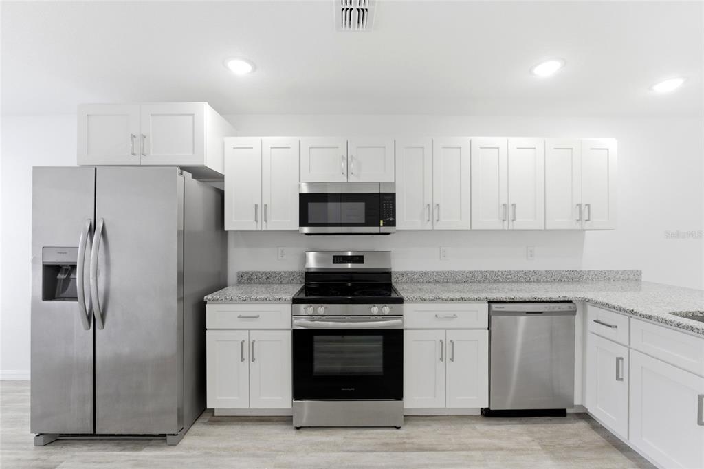 A kitchen with white cabinets, stainless steel appliances, and speckled granite countertops — 302 AVENUE P NW, WINTER HAVEN, FL