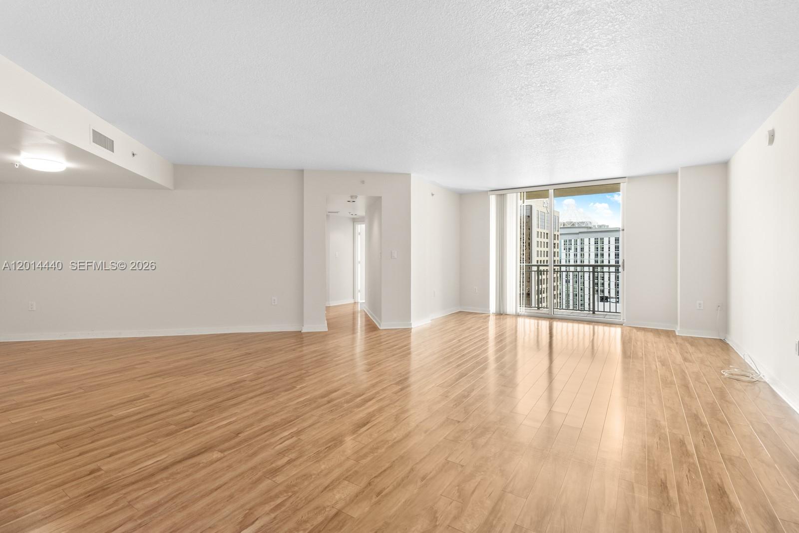 An empty living room features light wood-look flooring, white walls, and a sliding glass door — 9055 SW 73rd Ct # 1506, Miami FL 33156, MIAMI, FL