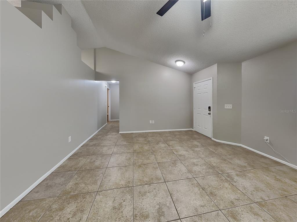 An empty room with light gray walls, tile flooring, a vaulted ceiling, and a white door — 1488 COUNTRY MANSION COURT, APOPKA, FL