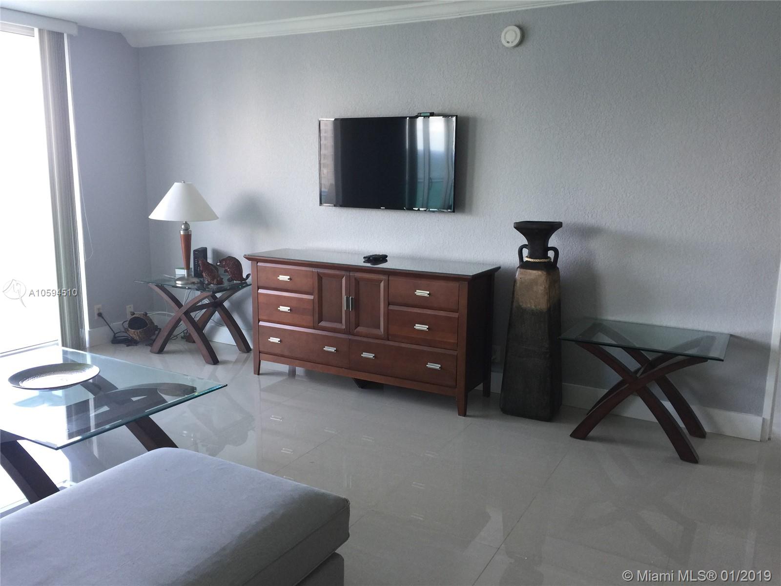 A living room features a wall-mounted television, a wooden dresser, and glass-topped side tables — 3901 S Ocean Dr # 14E, Hollywood FL 33019, HOLLYWOOD, FL
