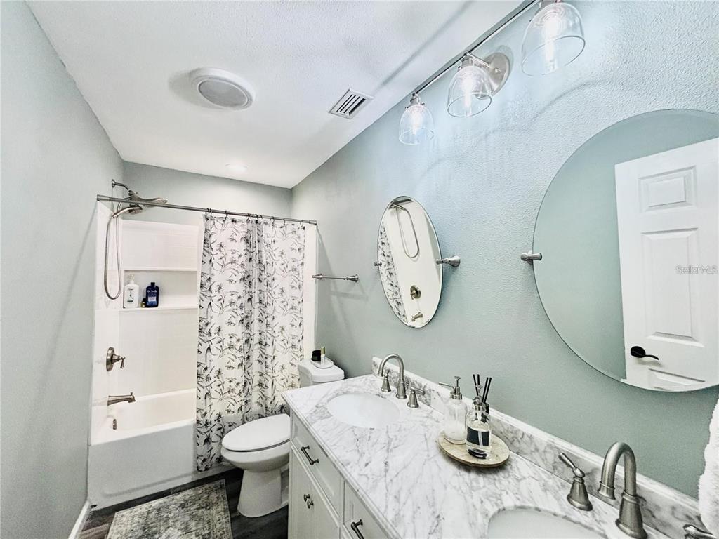 A bathroom features a double vanity with a marble countertop, two round mirrors, and a tub-shower — 4033 W 13, BRADENTON, FL