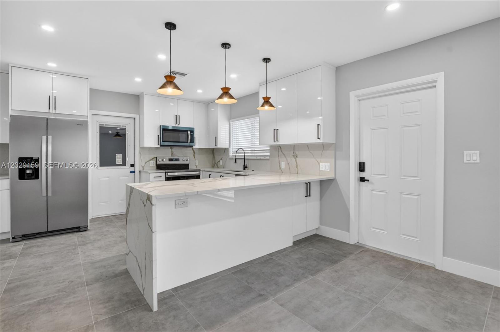 A modern kitchen features white glossy cabinets, marble-patterned countertops, and a central island — 1320 SE 10th St, Deerfield Beach FL 33441, DEERFIELD BEACH, FL