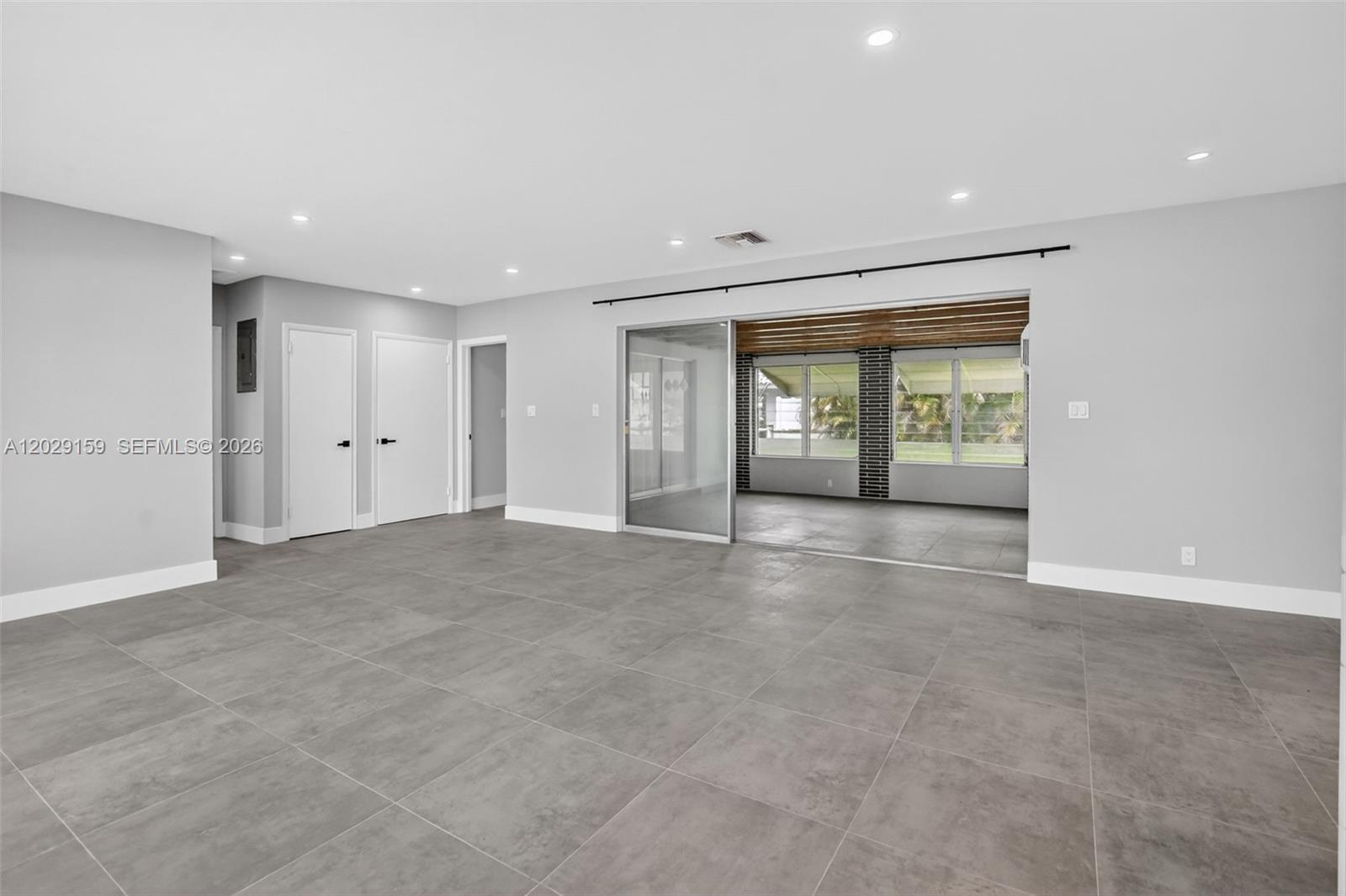A spacious room features large gray floor tiles, white walls, and a glass sliding door — 1320 SE 10th St, Deerfield Beach FL 33441, DEERFIELD BEACH, FL