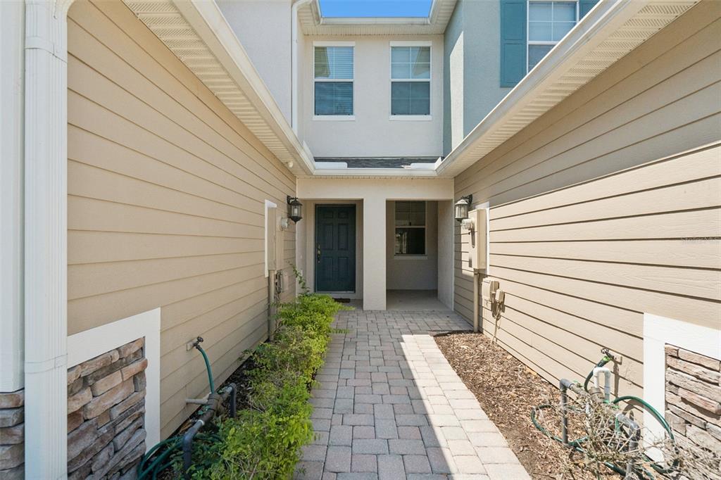 A paved walkway leads to the front entrance of a two-story tan townhouse — 15514 CAMPDEN STREET, WINTER GARDEN, FL