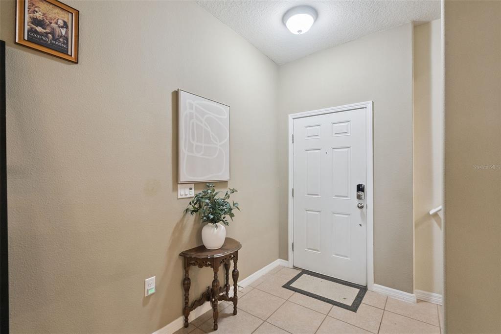 An entryway features a white door, tiled flooring, a small wooden table, and wall art — 15514 CAMPDEN STREET, WINTER GARDEN, FL