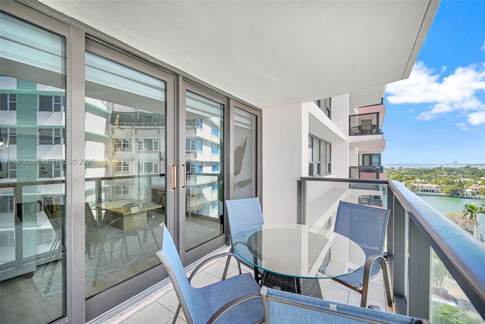 A balcony with a glass-topped table and four chairs overlooks the ocean and a building — 5225 Collins Ave # 1214, Miami Beach FL 33140, MIAMI BEACH, FL