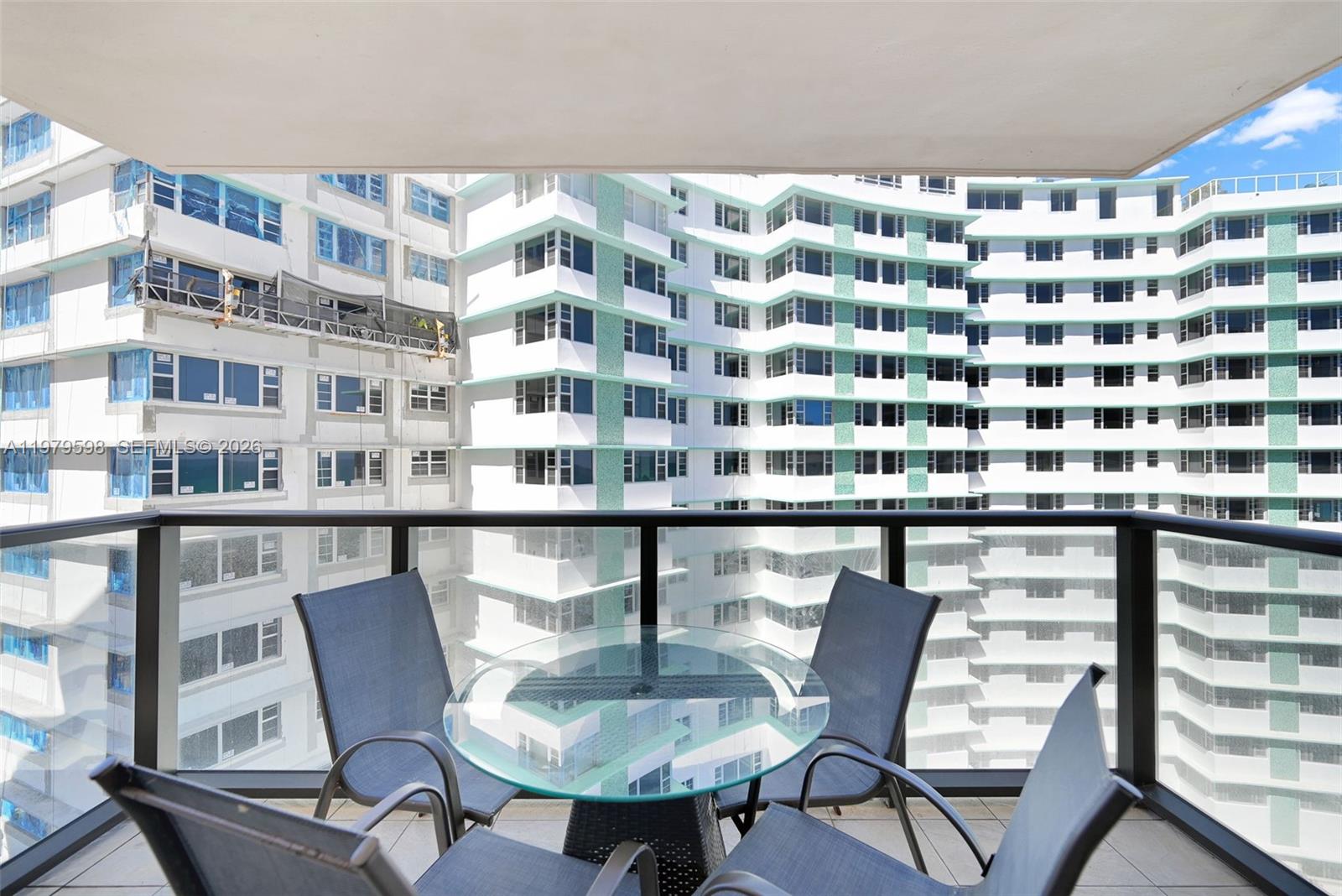 A balcony features a glass-topped table, four blue chairs, and sliding glass doors — 5225 Collins Ave # 1214, Miami Beach FL 33140, MIAMI BEACH, FL