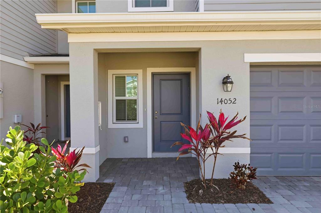 The exterior of a house features a gray front door, a paved walkway, and landscaping — 14052 LILAC SKY TERRACE, BRADENTON, FL