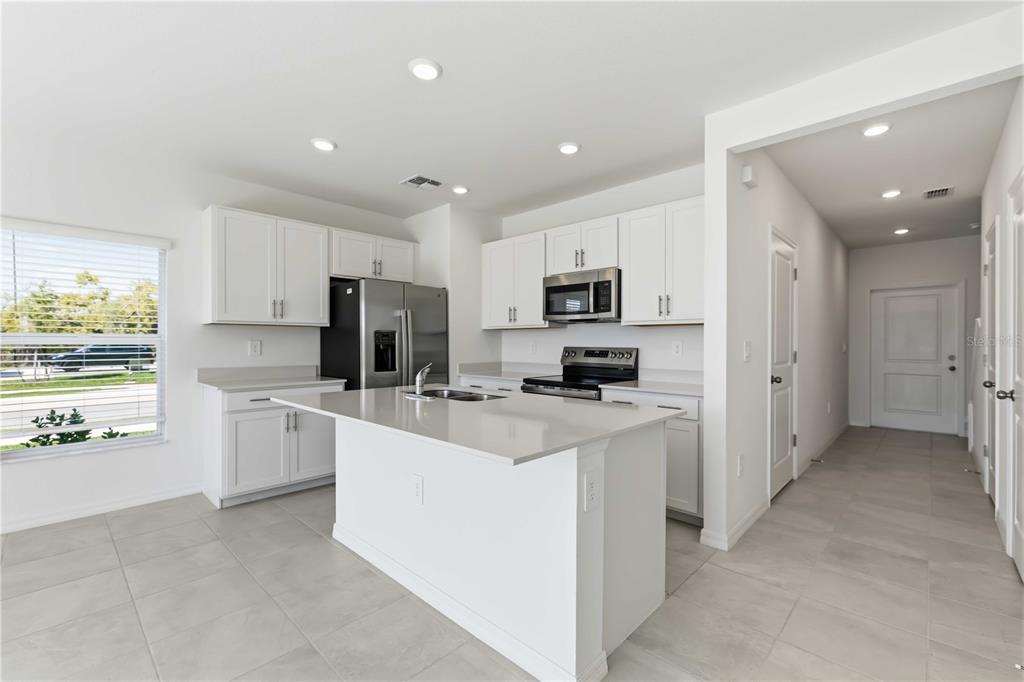 A modern kitchen features white cabinets, stainless steel appliances, a center island, and tile flooring — 14052 LILAC SKY TERRACE, BRADENTON, FL