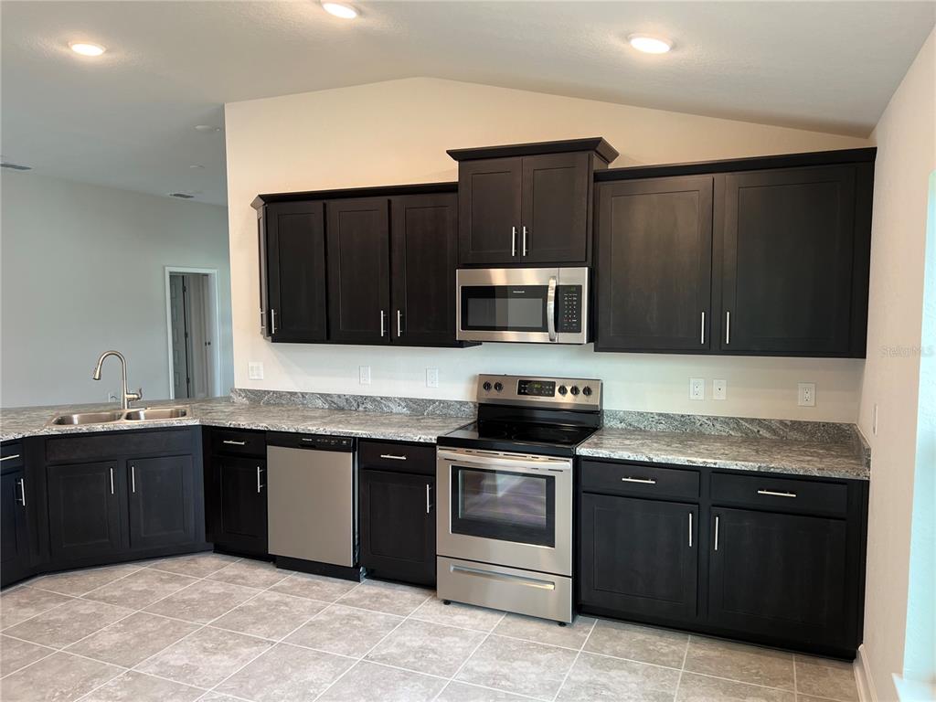 A kitchen features dark wood cabinets, stainless steel appliances, and gray granite countertops — 132 BERGAMOT LOOP, DAVENPORT, FL