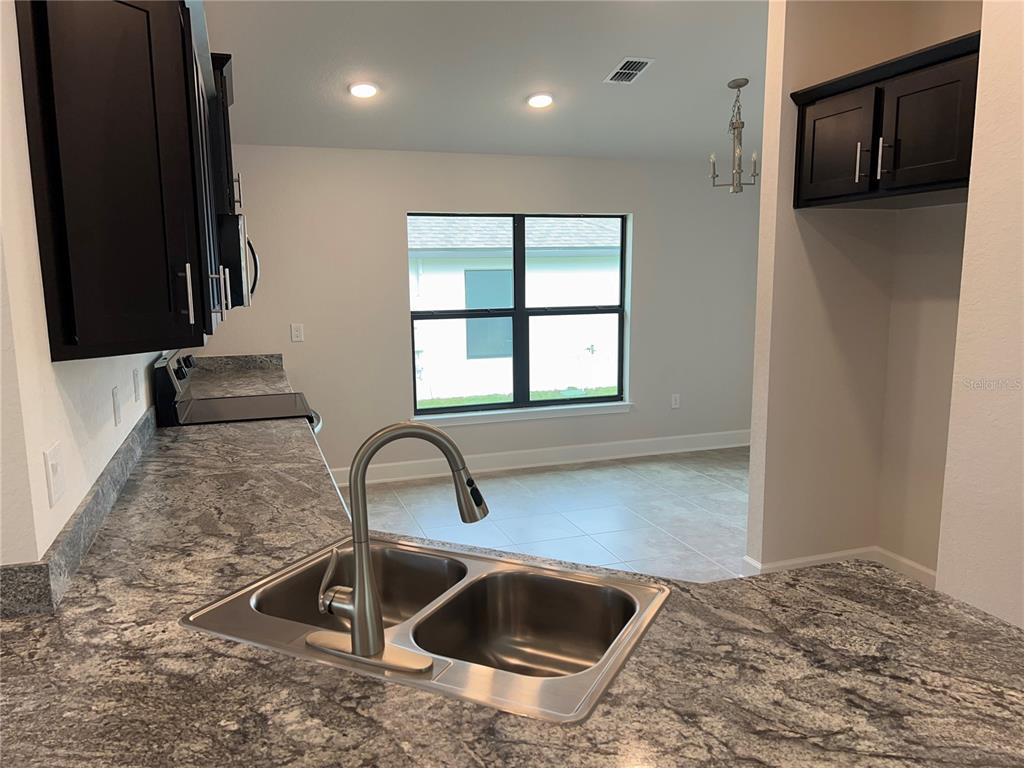 A kitchen features dark cabinets, granite countertops, a stainless steel sink, and a dining area — 132 BERGAMOT LOOP, DAVENPORT, FL