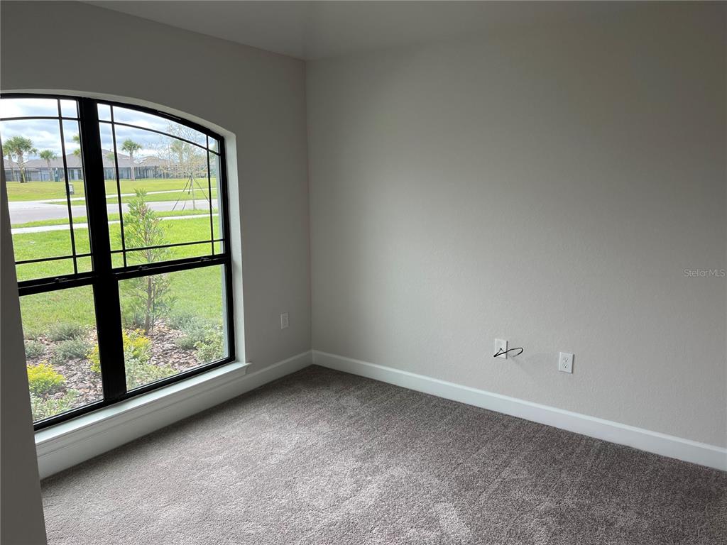 An empty bedroom features gray carpet, neutral walls, and a large arched window — 132 BERGAMOT LOOP, DAVENPORT, FL