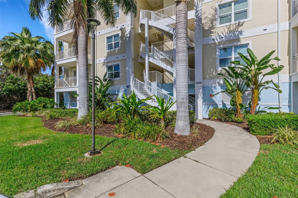A multi-story apartment building features exterior staircases, palm trees, and a concrete walkway — 3450 77TH STREET W UNIT 201, BRADENTON, FL