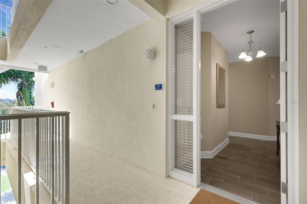 An exterior walkway leads to the open doorway of a unit labeled 201 — 3450 77TH STREET W UNIT 201, BRADENTON, FL