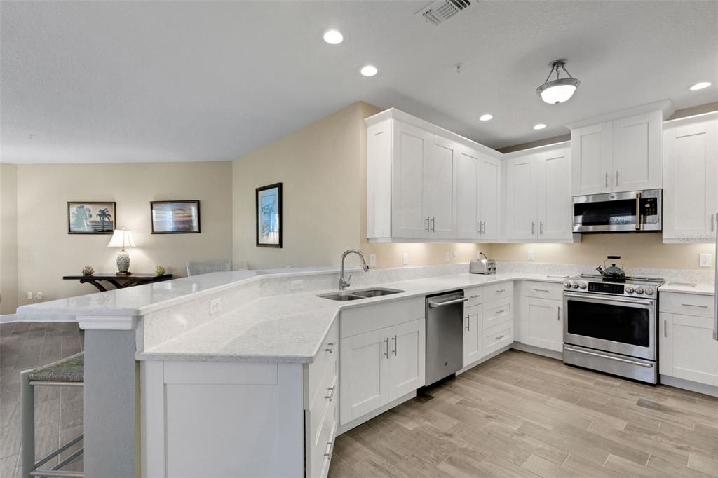 A kitchen with white cabinets, stainless steel appliances, and a light-colored quartz countertop island — 3450 77TH STREET W UNIT 201, BRADENTON, FL