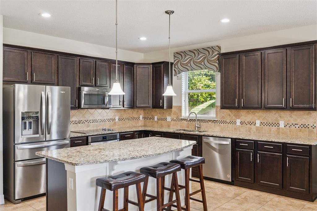 A kitchen with dark wood cabinets, granite countertops, stainless steel appliances, and a center island — 2651 MEAD AVENUE, ST CLOUD, FL