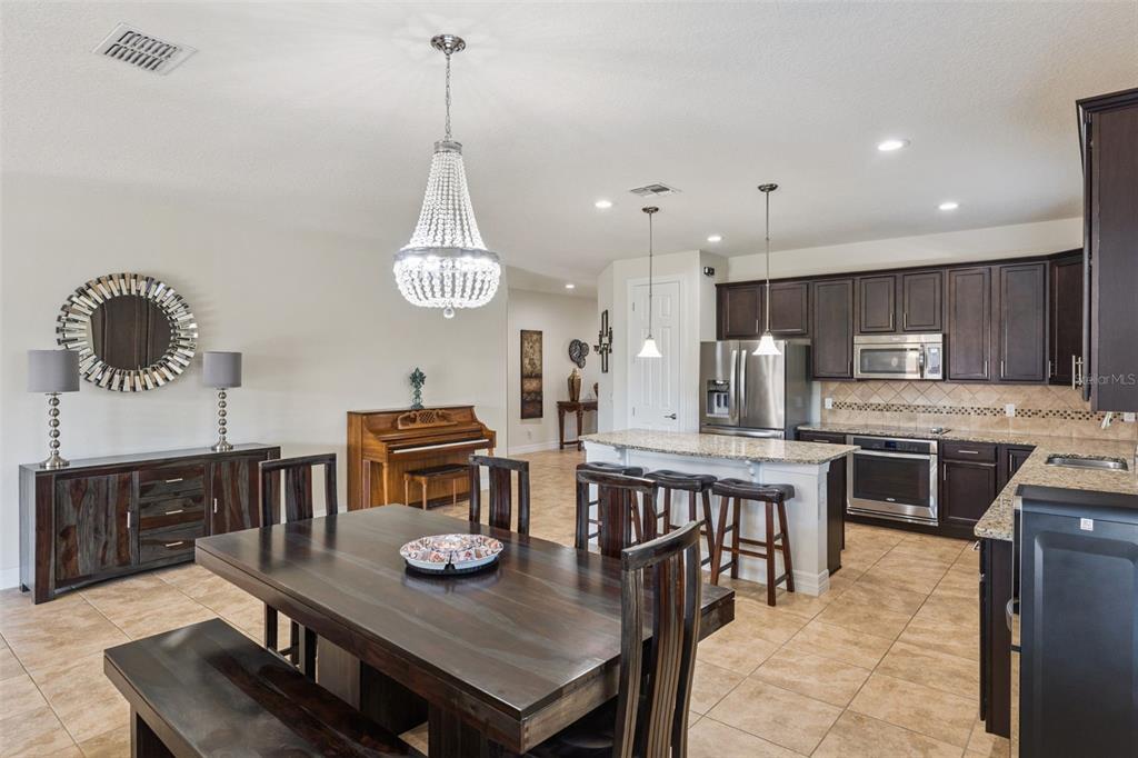 A dining area with a wooden table and piano flows into a kitchen with dark cabinets — 2651 MEAD AVENUE, ST CLOUD, FL