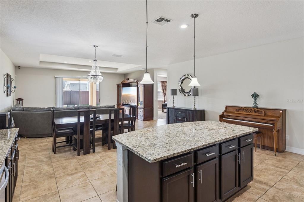 A kitchen island with granite countertops sits in front of a dining area and piano — 2651 MEAD AVENUE, ST CLOUD, FL