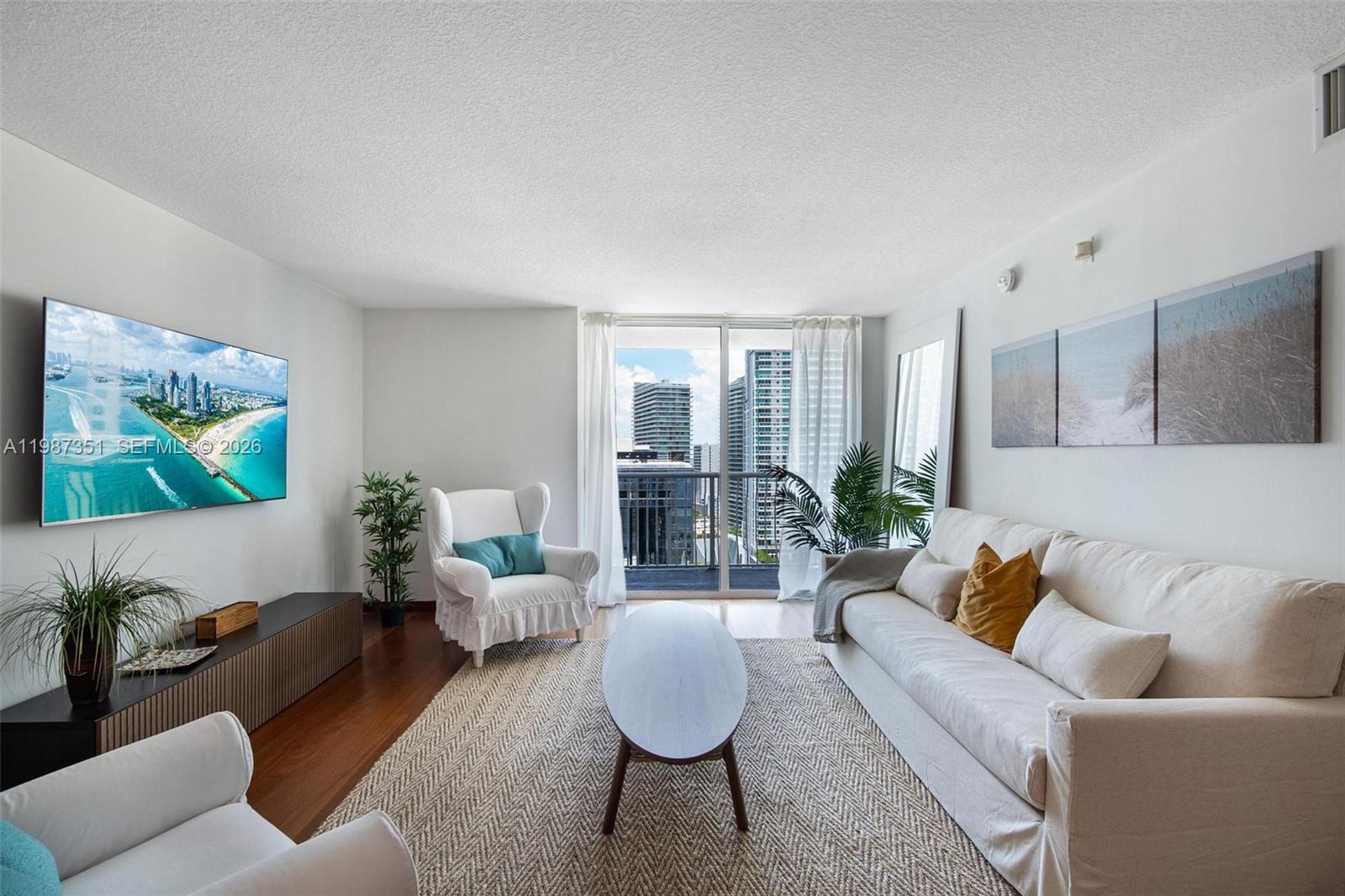 A living room features a white sofa, armchair, coffee table, and a balcony with city views — 1200 Brickell Bay Dr # 2824, Miami FL 33131, MIAMI, FL