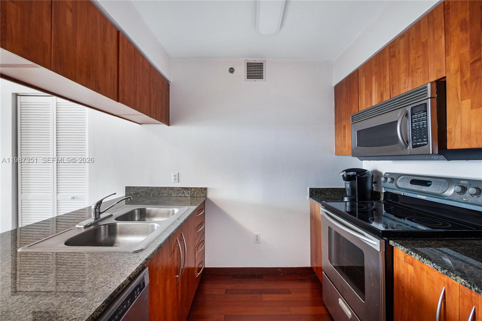 A galley kitchen features wood cabinets, granite countertops, and stainless steel appliances — 1200 Brickell Bay Dr # 2824, Miami FL 33131, MIAMI, FL