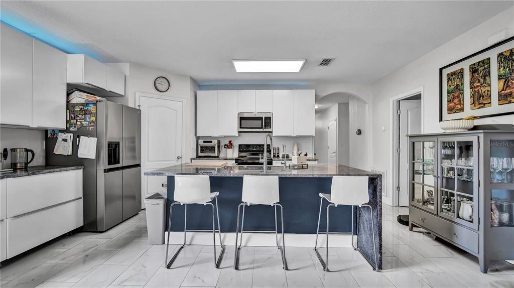 A modern kitchen features white cabinetry, a dark blue island with three stools, and tile flooring — 1576 DIAMOND LOOP DRIVE, KISSIMMEE, FL