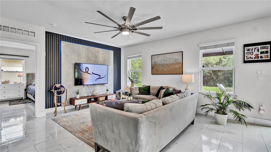A modern living room features a large gray sectional, a wall-mounted television, and tile flooring — 1576 DIAMOND LOOP DRIVE, KISSIMMEE, FL