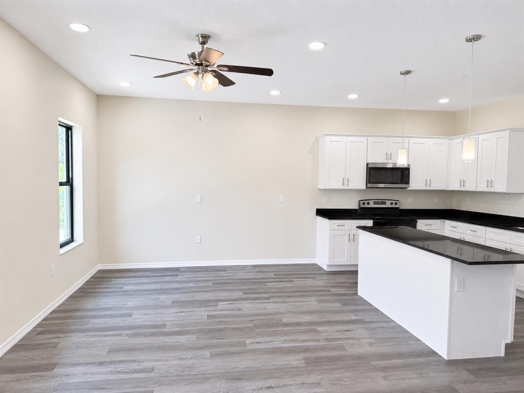 A kitchen with white cabinets, black countertops, and a ceiling fan in an open area — 4349 CAMBIO GARDENS CT, TAMPA, FL