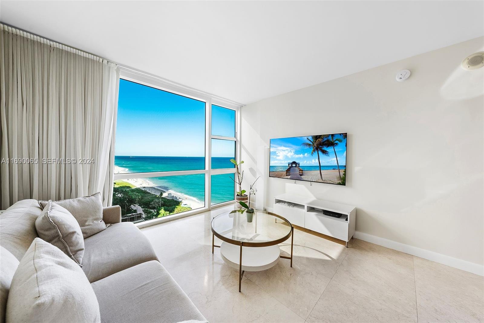 A living room features a beige sofa, glass coffee table, and floor-to-ceiling ocean views — 6801 Collins Ave # 1203, Miami Beach FL 33141, MIAMI BEACH, FL