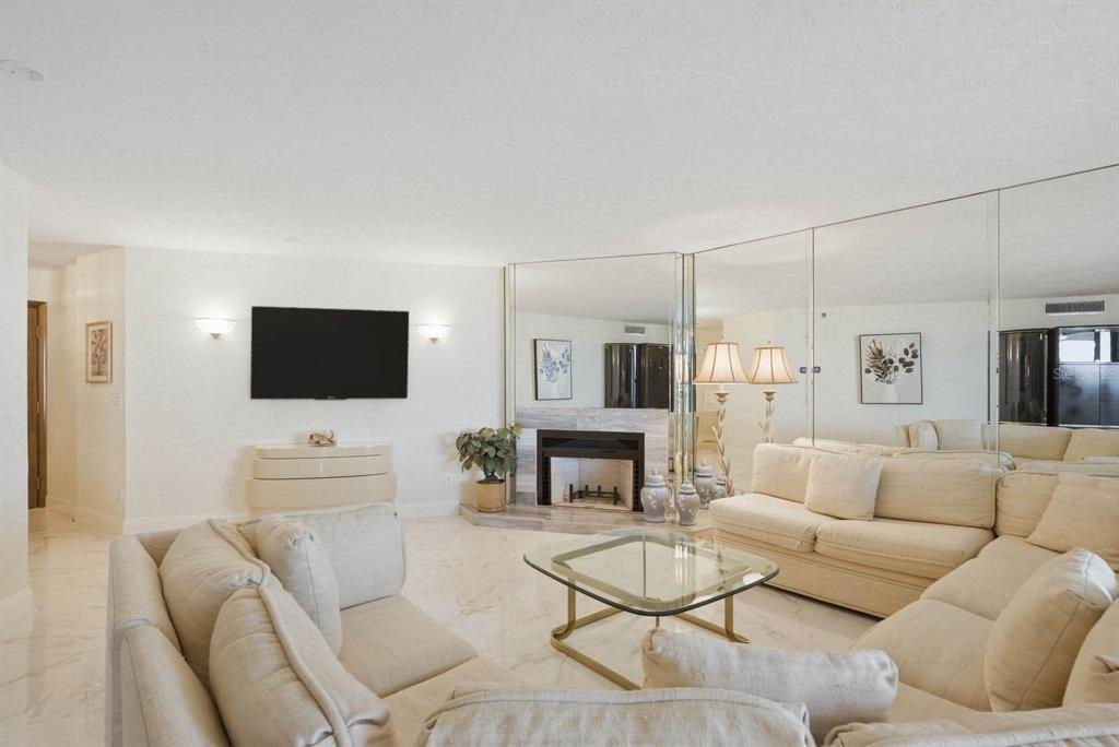 A living room features white sofas, a glass coffee table, a fireplace, and mirrored walls — 1600 GULF BOULEVARD UNIT 817, CLEARWATER BEACH, FL