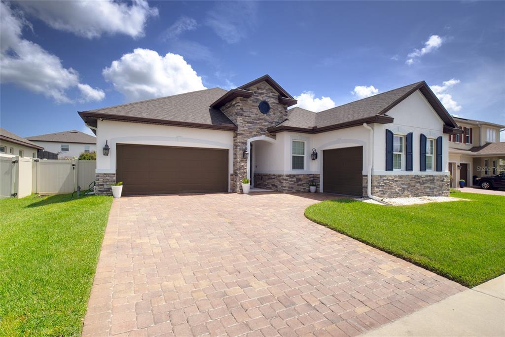 A single-story house with a stone facade, brown garage doors, and a paved driveway — 443 WRANGLER ROAD, WINTER GARDEN, FL