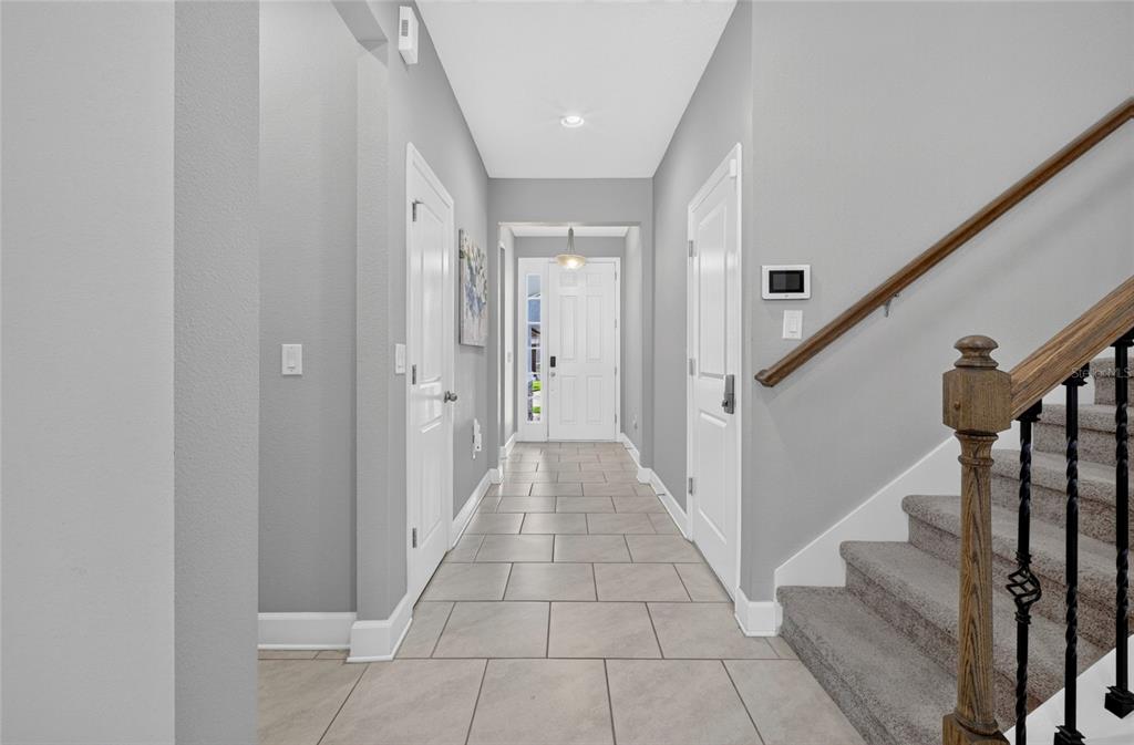 A tiled entryway features a staircase with a wooden railing and a white front door — 443 WRANGLER ROAD, WINTER GARDEN, FL