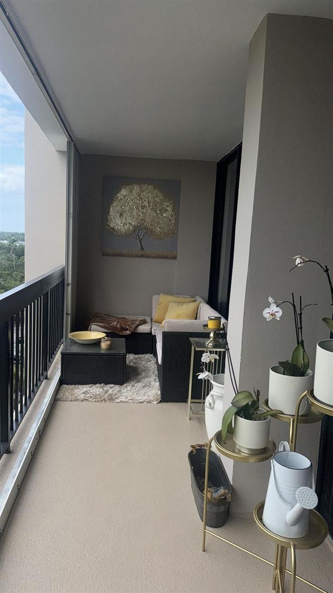 A covered balcony features a wicker sectional sofa, a small coffee table, and potted orchids — 2425 Presidential Way # 705, West Palm Beach FL 33401, WEST PALM BEACH, FL