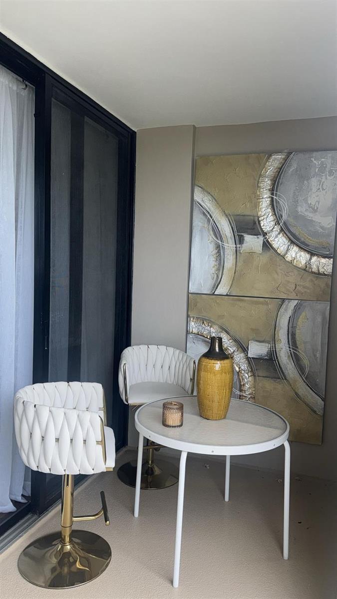 A small balcony features two white woven bar stools, a round table, and wall art — 2425 Presidential Way # 705, West Palm Beach FL 33401, WEST PALM BEACH, FL
