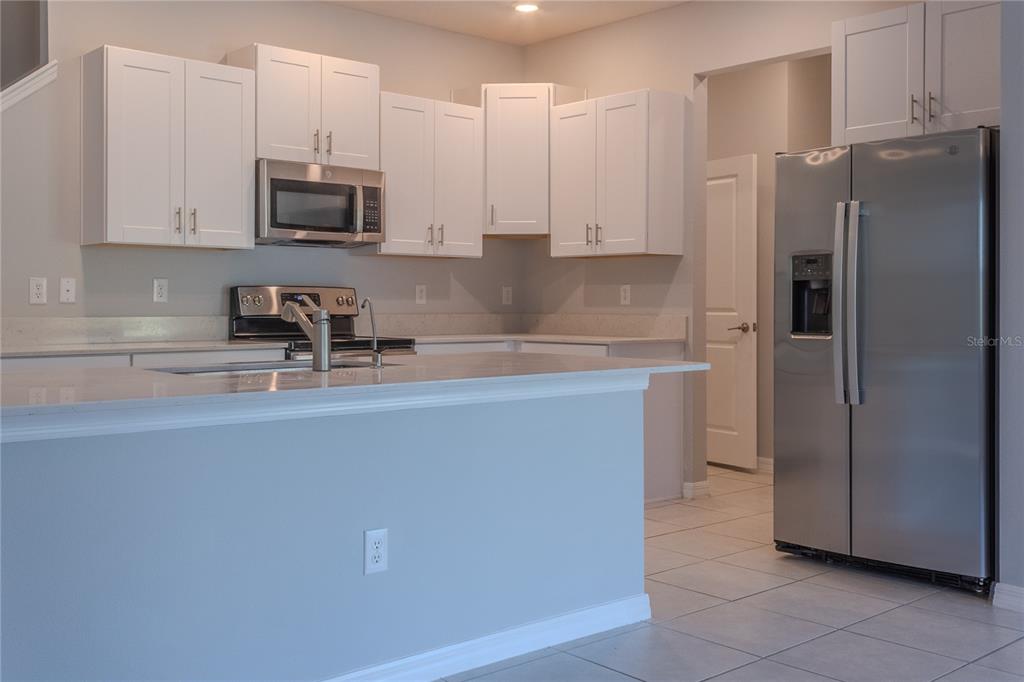A kitchen features white cabinets, stainless steel appliances, and a light-colored countertop island — 17711 NECTAR FLUME DRIVE, LAND O LAKES, FL