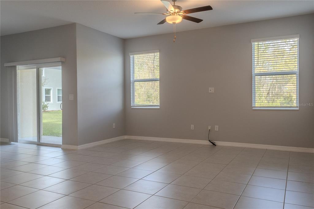 An empty living room features light-colored tile flooring, gray walls, two windows, and a ceiling fan — 17711 NECTAR FLUME DRIVE, LAND O LAKES, FL