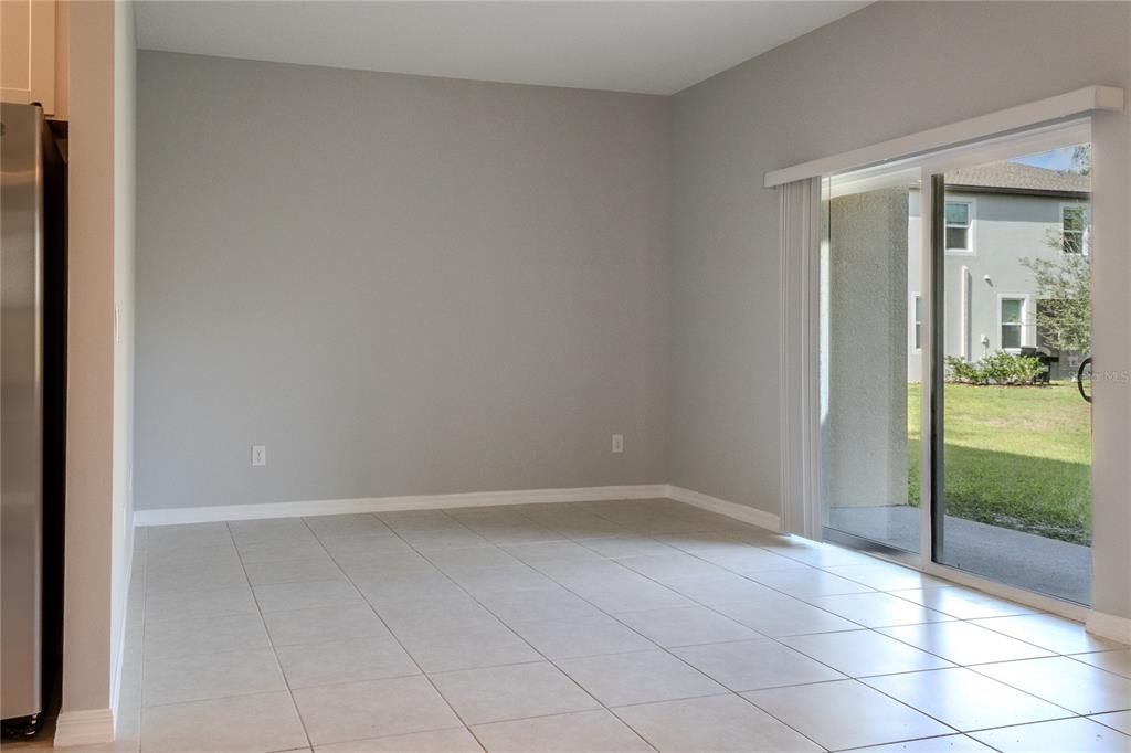 An empty dining area with light-colored tile flooring, gray walls, and a sliding glass door — 17711 NECTAR FLUME DRIVE, LAND O LAKES, FL