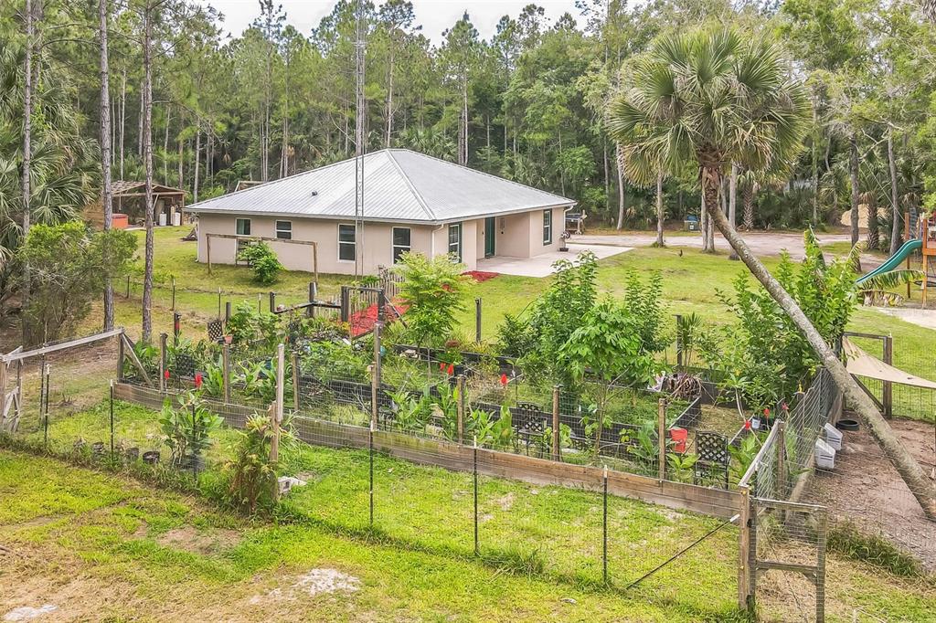 An exterior view of a single-story house with a metal roof and a fenced garden — 723 RIVER RUN ROAD, OSTEEN, FL