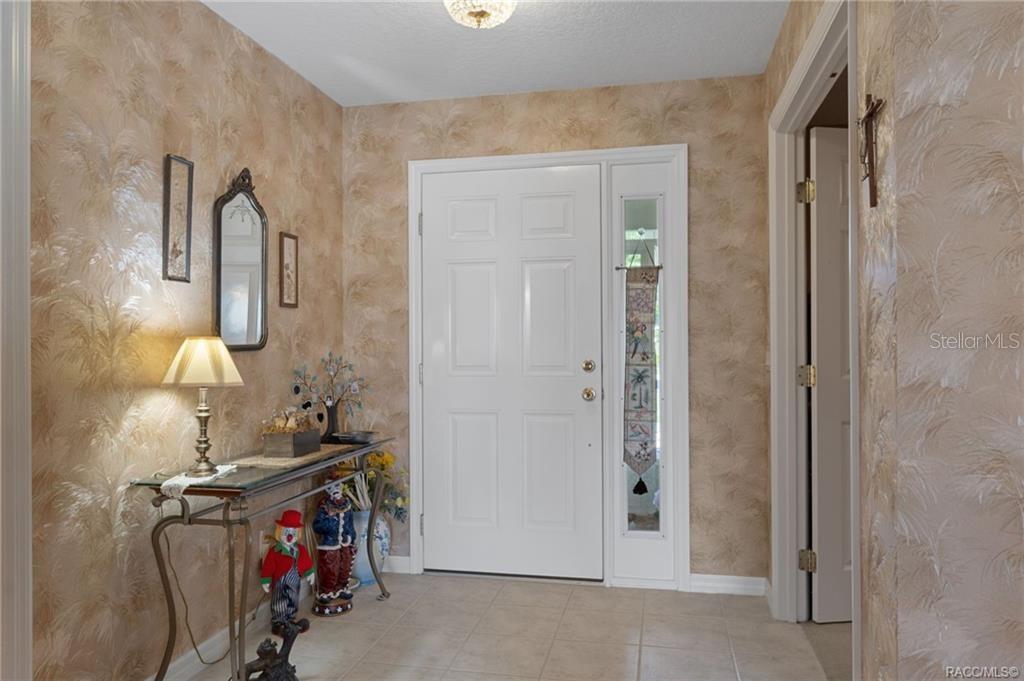 An entryway features beige textured wallpaper, a glass-topped console table, and a white front door — 4658 N LAKE VISTA TRAIL, HERNANDO, FL