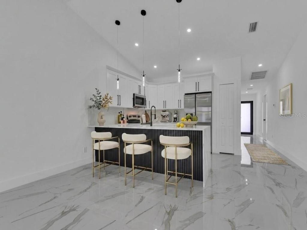 A modern kitchen features white cabinets, a black slatted island, and white marble-look tile flooring — 4745 13TH STREET SW, LEHIGH ACRES, FL