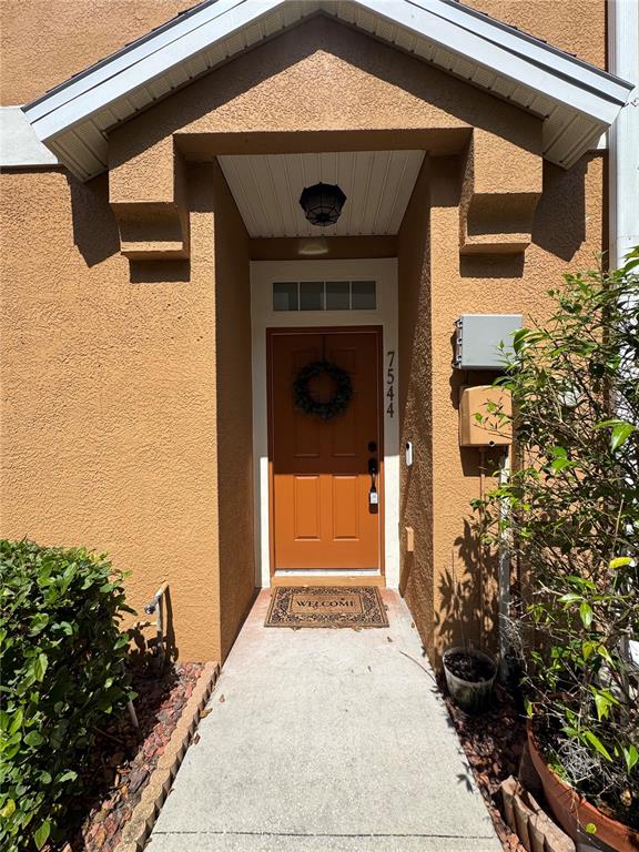 An orange front door with a wreath sits at the end of a concrete walkway — 7544 RED MILL CIRCLE, NEW PORT RICHEY, FL